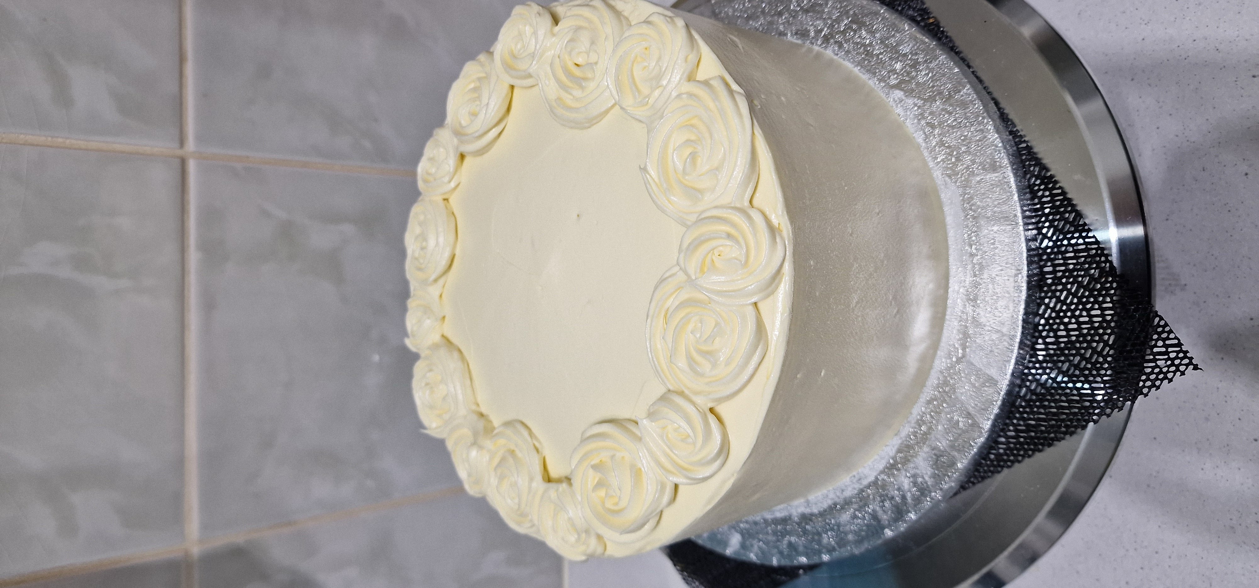 Elegant white chocolate buttercream cake decorated with beautifully piped icing roses around the top border, crafted by Fontaines Fancies in Greenford